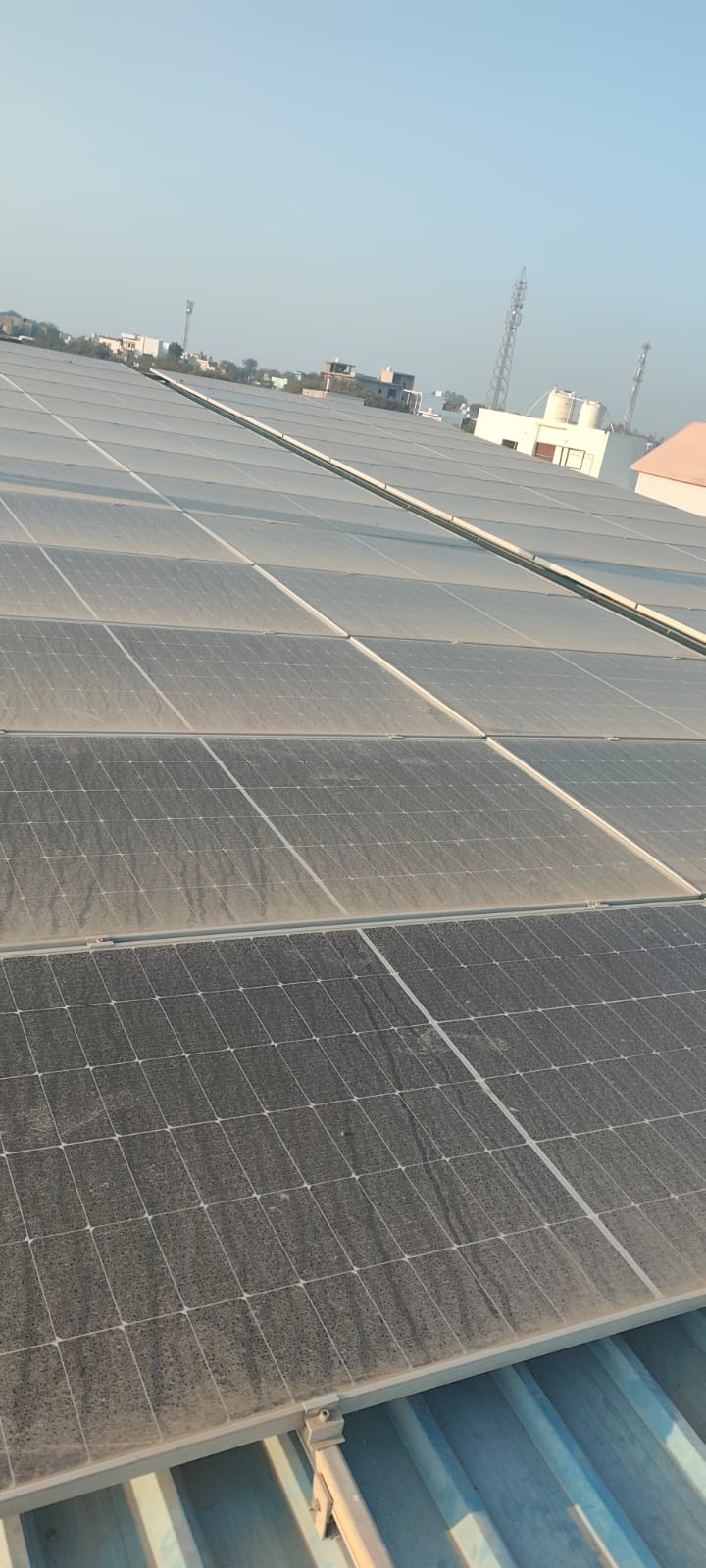 Rows of dusty solar panels installed on a rooftop under a clear sky, highlighting the need for maintenance.