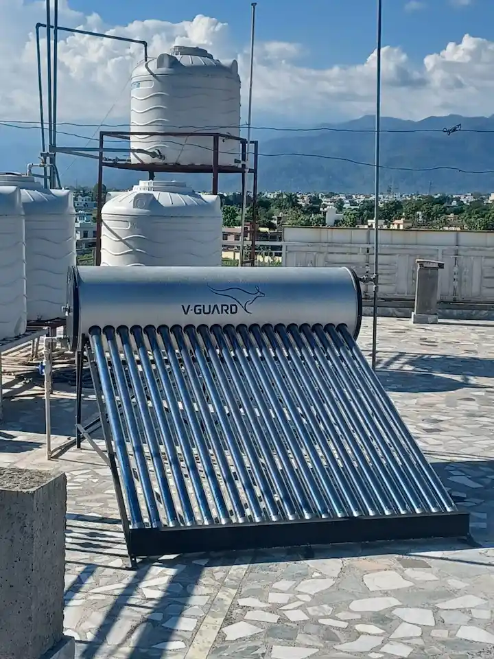 V-Guard solar water heater installed on a rooftop with white water tanks and mountain views in the background.